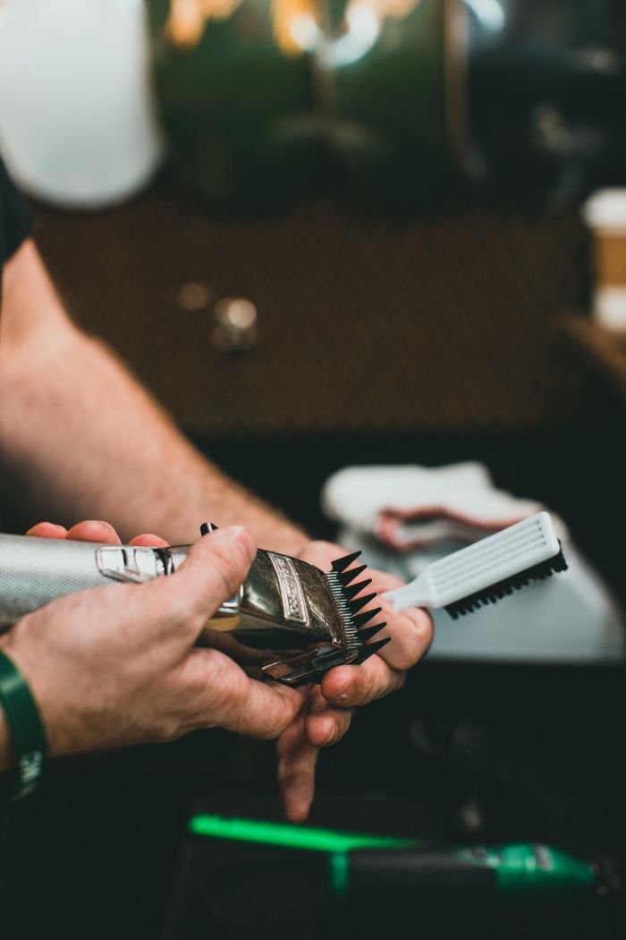 Close-up of a barber cleaning a hair clipper with a brush in a barbershop.