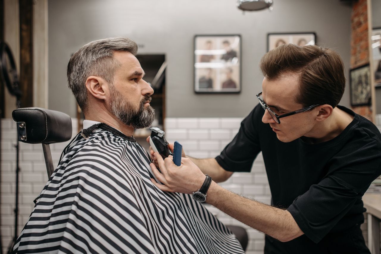 A professional barber precisely trimming a client's beard in a modern barbershop.